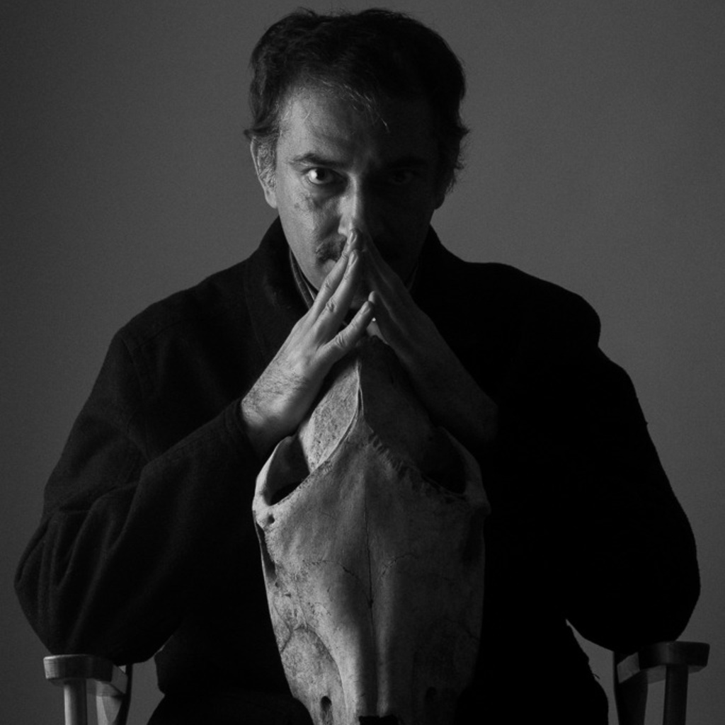 In black and white, Mohsen Emadi holds an animal skull in his lap and stares into the camera
