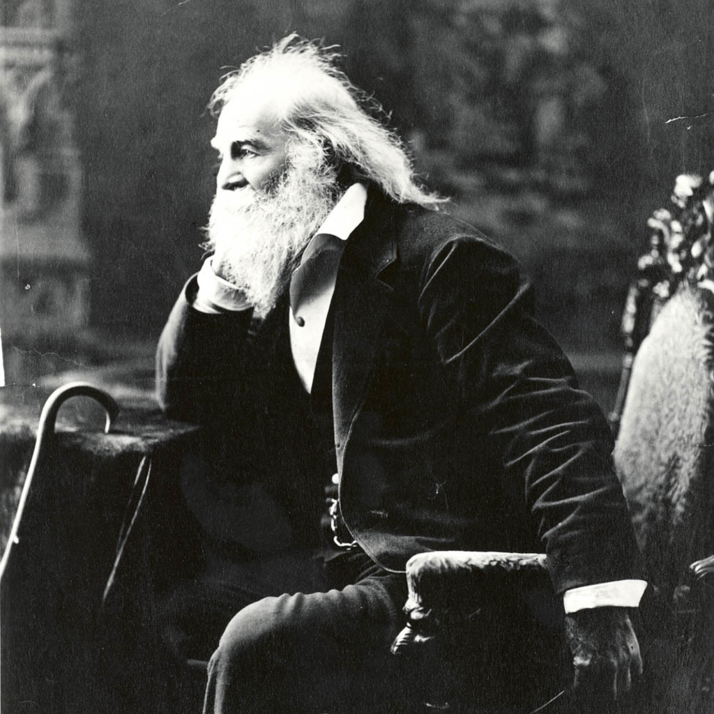 A black and white photo of Walt Whitman sitting in a chair and facing the left