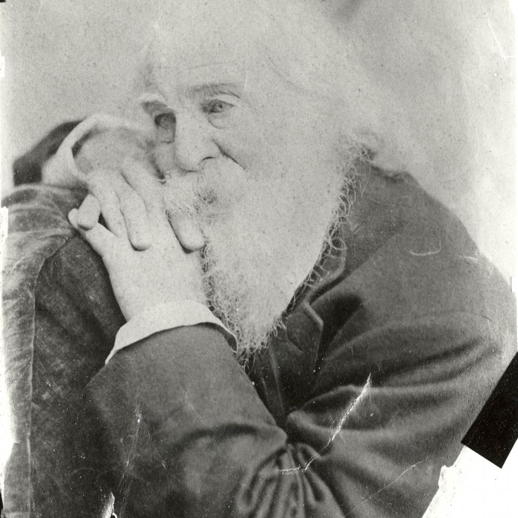 An aged black and white photo of Walt Whitman resting his head in his hands and looking to the right