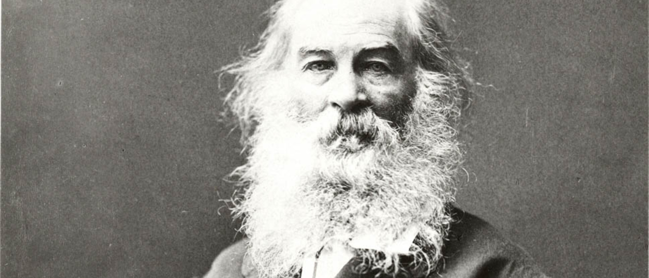 A black and white photo of Walt Whitman sitting with his arm folded in his lap and staring into the camera